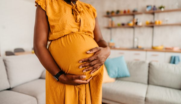 Portrait of beautiful pregnant black mother holding her pregnant belly at home. Close-up.